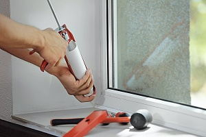 hands of a contractor caulking a window in a residence