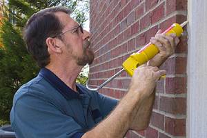 A person applying caulk on the exterior of his home