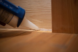 Interior caulking in progress. Applying silicone caulking between wood floor and wall