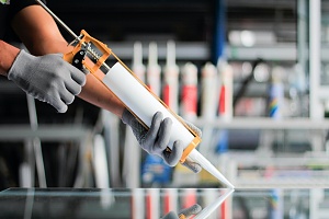man caulking a window wearing gloved and using a tool
