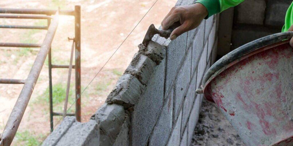 masonry worker make concrete wall by cement block and plaster at construction site