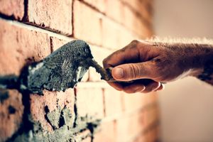 Man adding mortar between brick gaps with the help of brick trowel