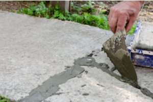 A man filling cracks of a concrete walkway with mortar