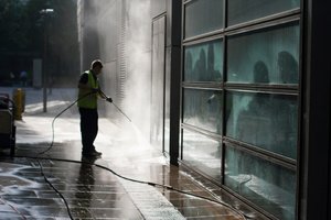 A man pressure washing a glass wall before waterproofing commercial building 