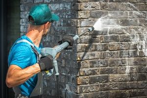 A man pressure washing a brick wall