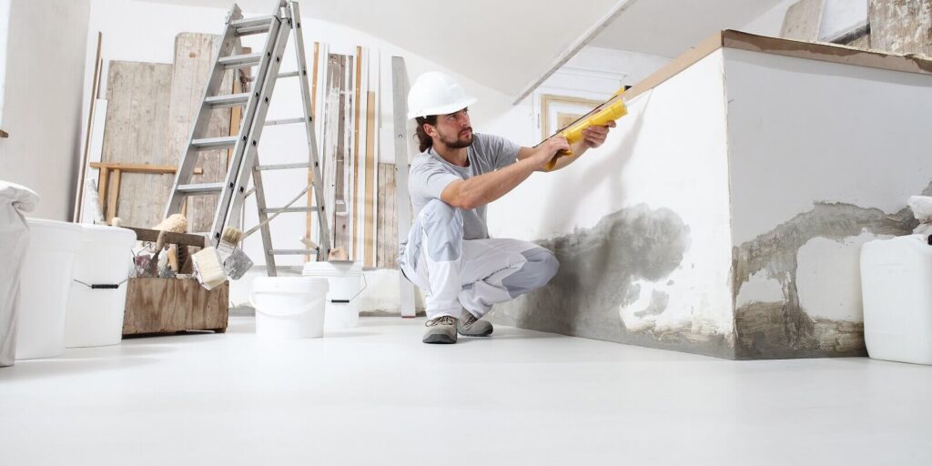 construction worker plasterer man uses caulking gun in building site of home renovation with tools and building materials on the floor