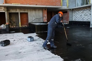 worker applies bitumen mastic to the foundation