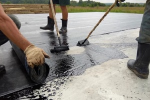 roofer worker painting bitumen praimer at concrete surface by the roller brush waterproofing