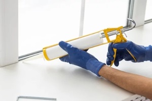 construction worker sealing window with caulk indoors