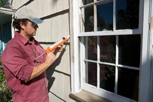 man in red shirt applying caulk to the windows