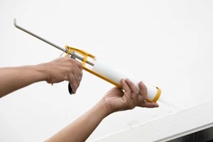 PA builders are using a silicone caulking gun to fill a leak between glass and aluminum