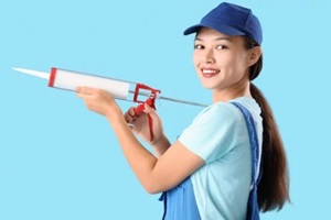 female asian plumber with caulking gun on blue background